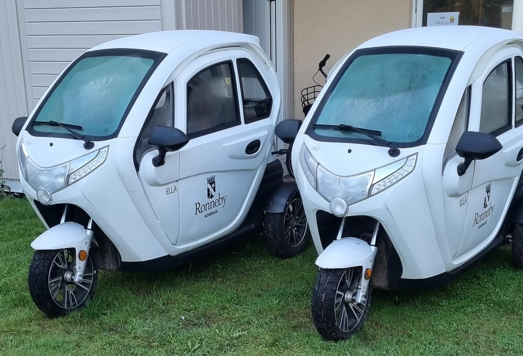Två el-mopedbilar står uppställda sida vid sida framför ett Vård- och omsorgsboende