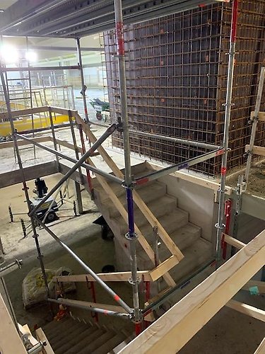 Byggarbetsplats med ny trappa i betong och säkerhetsställningar 