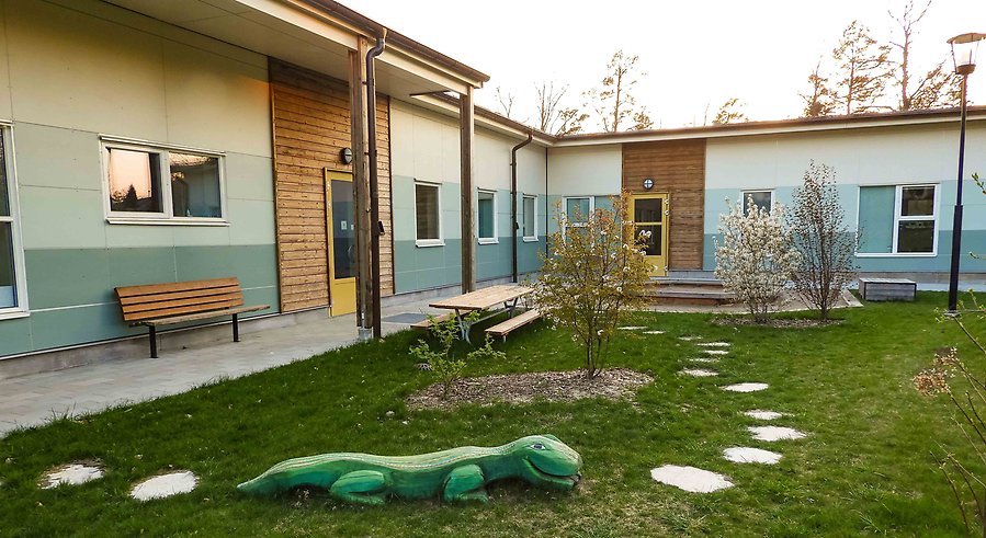 Del av byggnad för förskola och en utemiljö med gräs och buskar